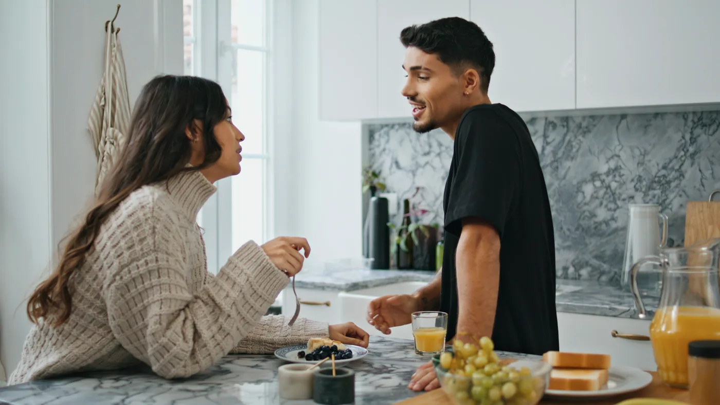 Two people smile and talk across a kitchen counter.