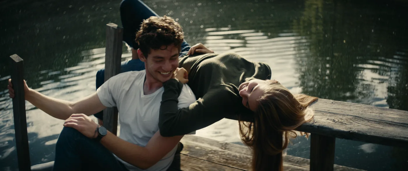 Two people laugh together on a pier beside the water.