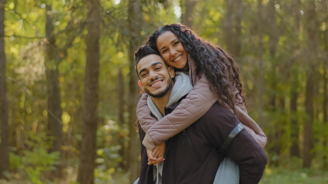 A couple laughing together on a piggyback ride in the forest