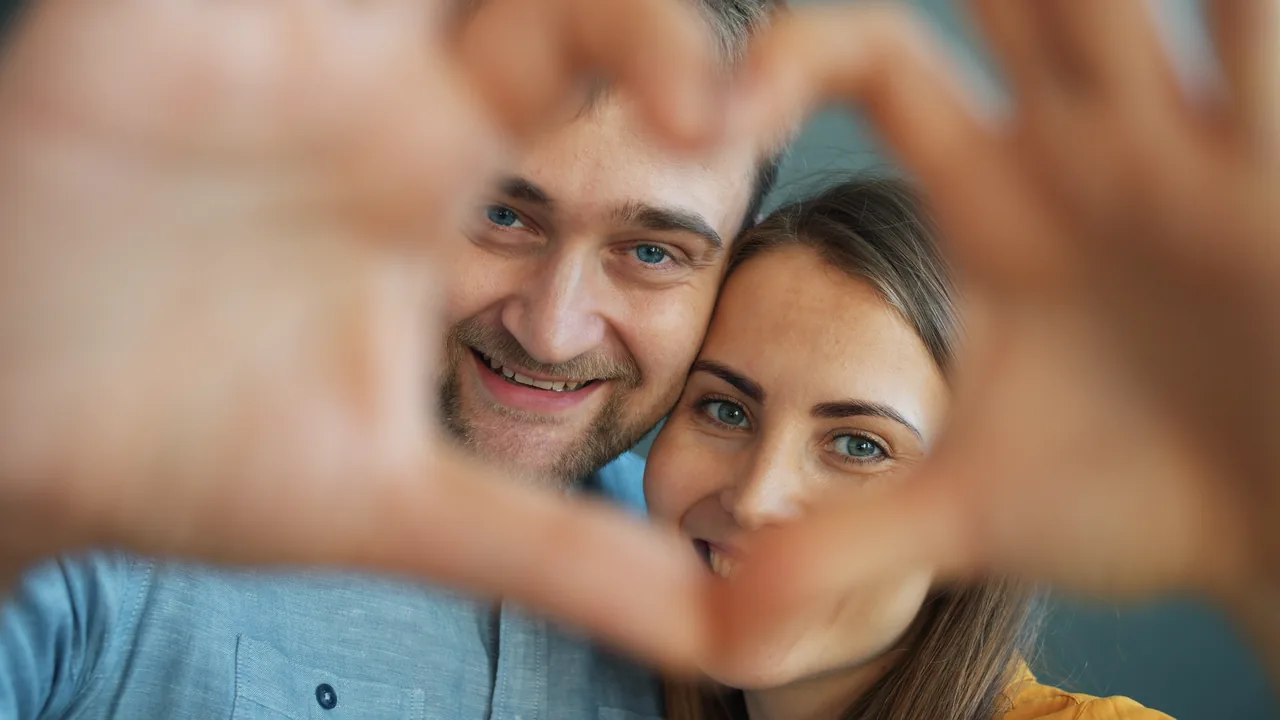 A smiling couple framing their faces with a heart made by their hands